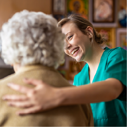 Pflegerin lächelt eine ältere Dame an und legt ihr eine Hand auf den Rücken